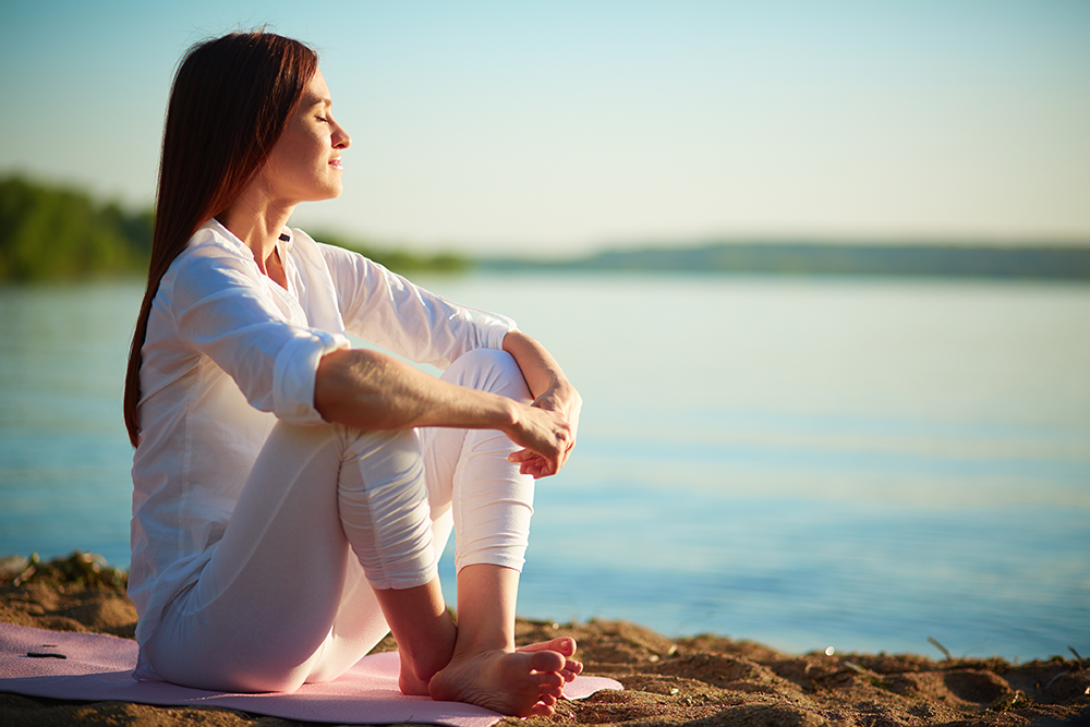 Side view of serene woman sitting on sandy beach against blue sky outdoors