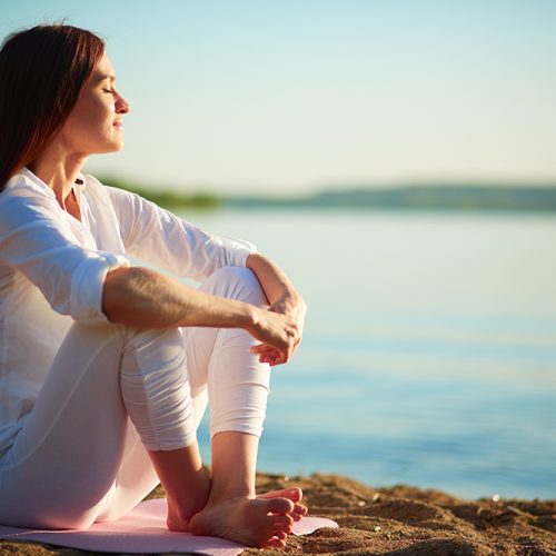 Side view of serene woman sitting on sandy beach against blue sky outdoors