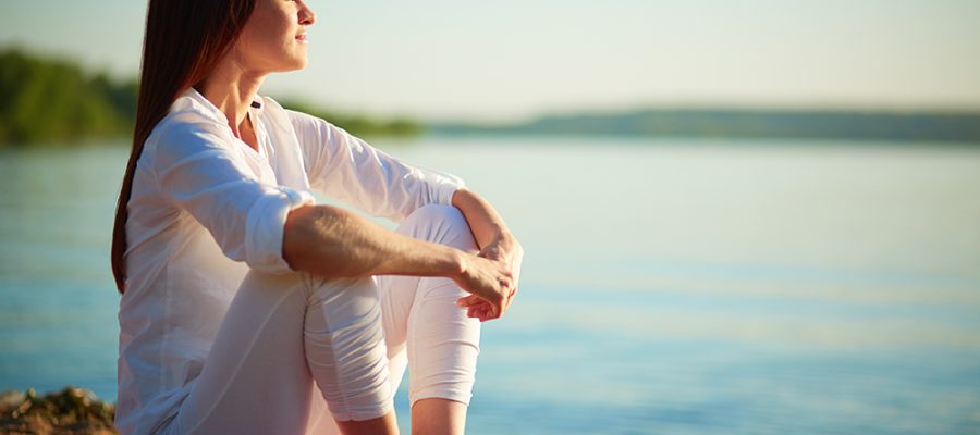 Side view of serene woman sitting on sandy beach against blue sky outdoors